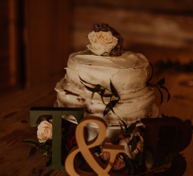 Small two tier rustic wedding cake with rose decor and initials of the couple's names