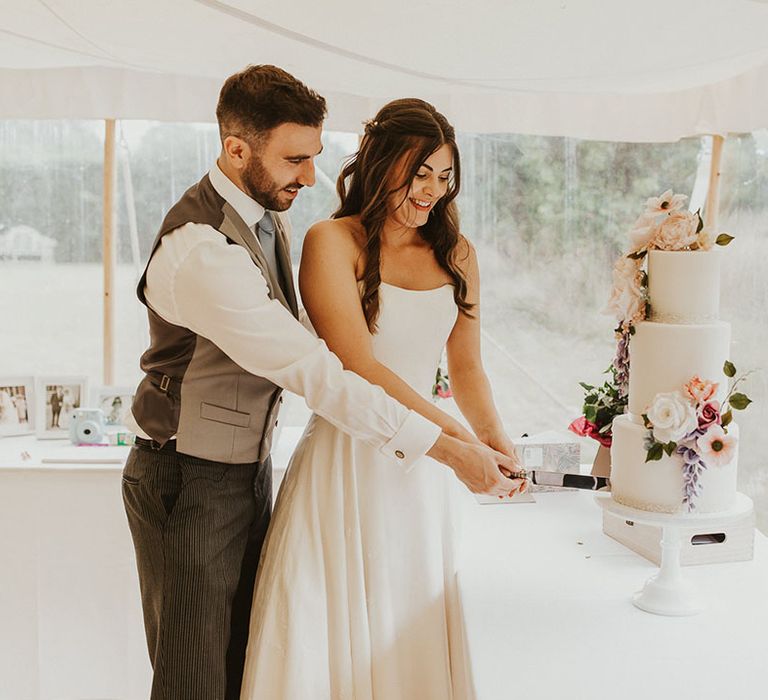 Bride and groom cut their white iced three tier wedding cake decorated with pink and purple wedding flower decor 