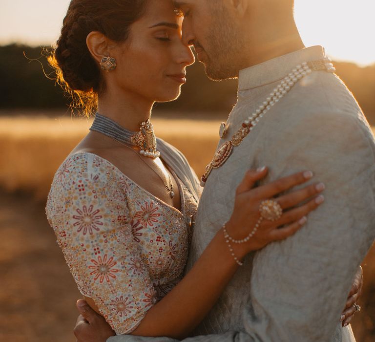 Groom wears pearl embellished necklace and grey sherwani whilst stood with his bride during golden hour