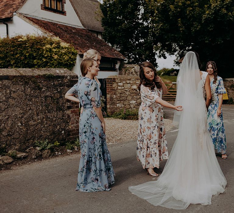 Bridesmaids in mixed floral dresses adjust bride's veil