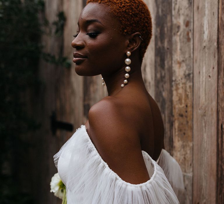 Bride in off shoulder wedding dress with long lace puff sleeves and pearl drop earrings