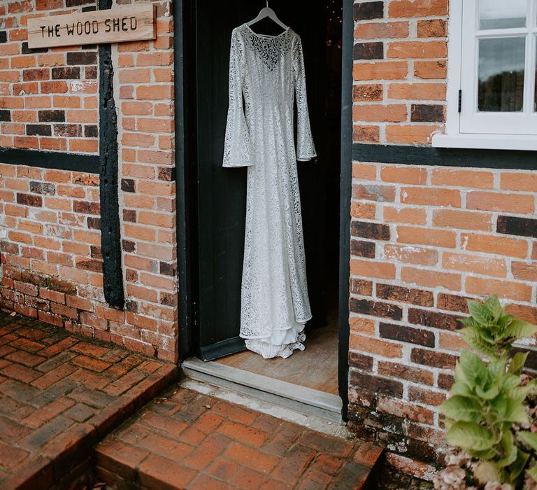 Bride's long sleeve laser cut lace wedding dress hanging on the doorframe 