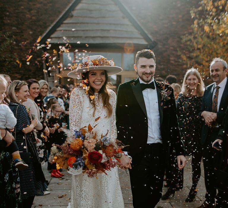 Colourful confetti exit for the bride and groom with the bride in a laser cut lace wedding dress and groom in velvet tuxedo 