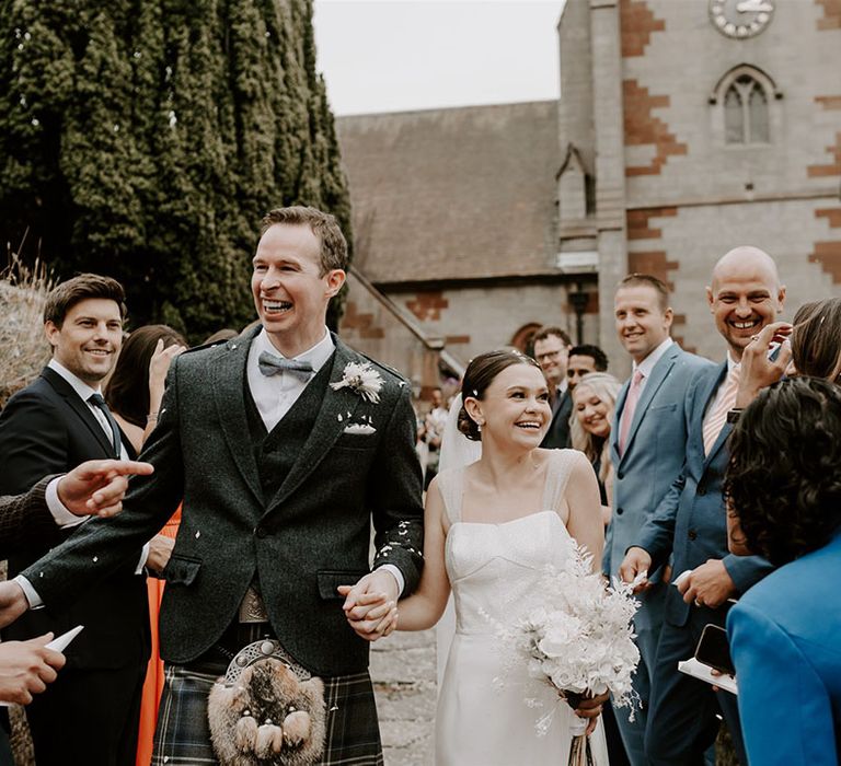 The bride and groom smile as the guests congratulate them and throw confetti over the couple 