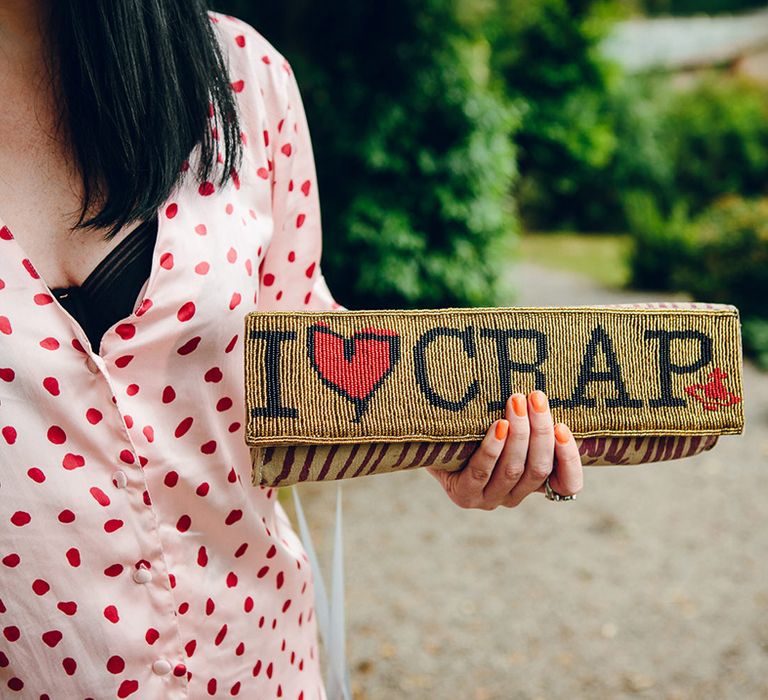 Bridesmaid holding golden Vivienne Westwood clutch with black and red lettering