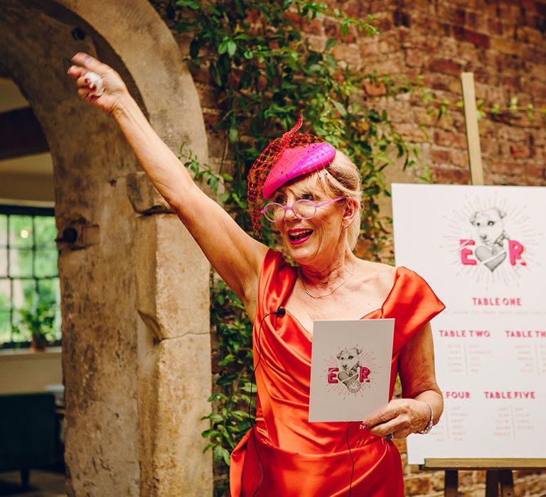 Mother of the bride wearing burnt orange sweetheart neckline satin dress with pink fascinator hat doing wedding speech