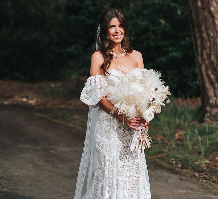 Bride in boho fitted lace wedding dress with train and detachable sleeves with dried white flower bouquet 