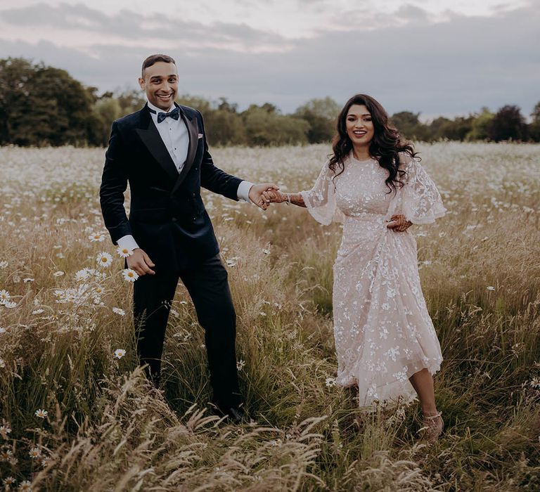 Bride in embellished Needle & Thread dress stands beside her groom in velvet tuxedo 