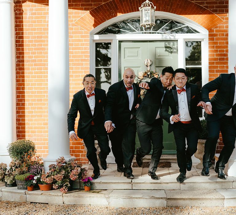 Groom & his groomsmen in black-tie jump from steps at Reymerston Hall 