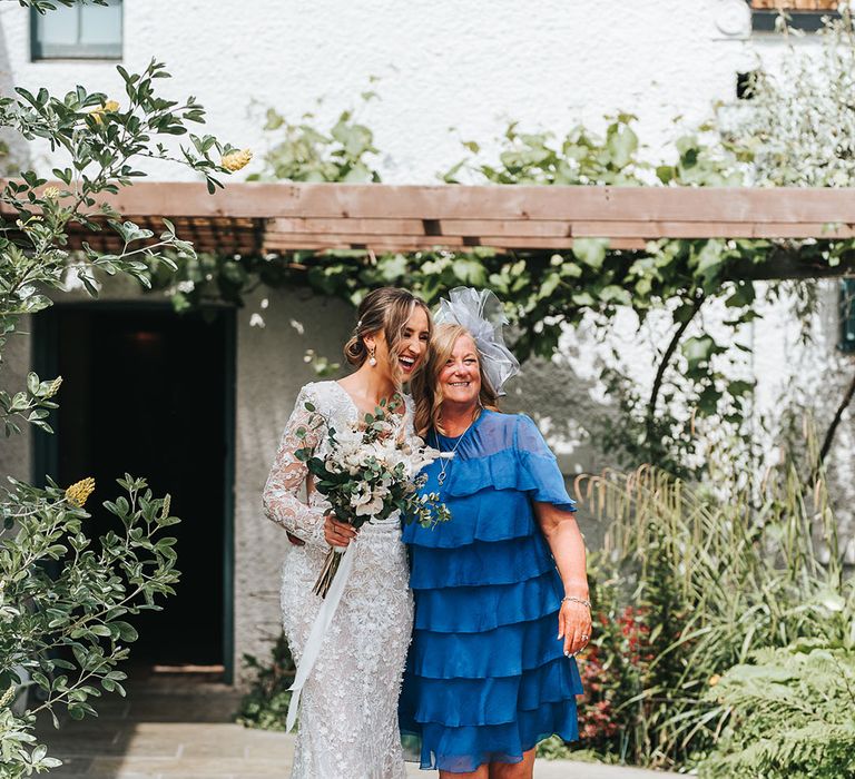 Wedding guest in electric blue ruffle dress with light blue fascinator walking with the bride in floral wedding dress with white flower bouquet 