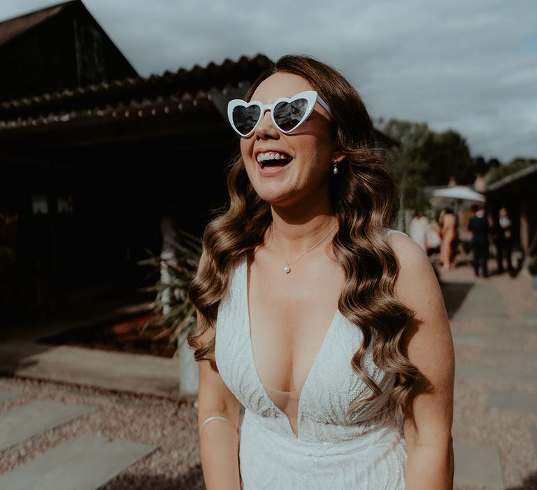 Bride laughing with brown hair in waves with a pearl necklace and white retro wedding sunglasses 