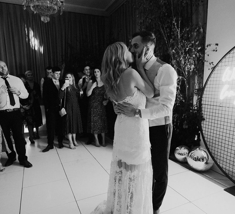 A neon light and disco ball decorate the dance floor with the bride and groom sharing their first dance together with a kiss 