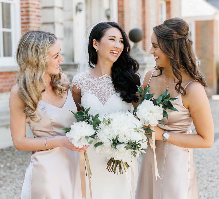 Bride and bridesmaid in pink satin dresses holding white flower bouquets 