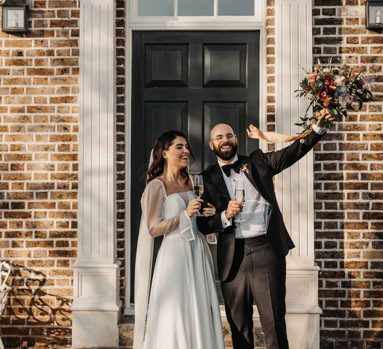 Bride in square neck puff sleeve wedding dress and long embroidered wedding veil standing with groom in classic black tuxedo with black bowtie 