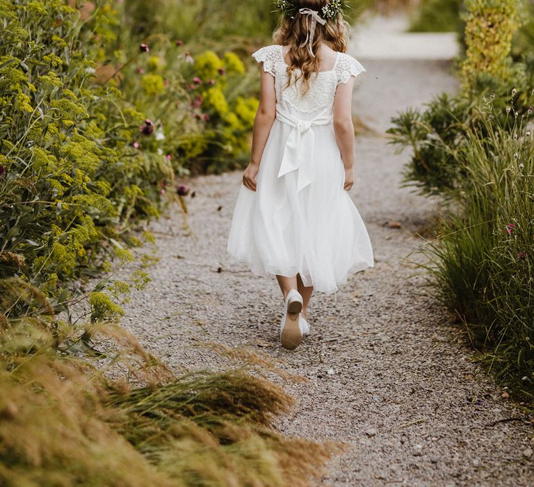 Flower girl wearing pretty white dress with a flower crown and white shoes for classic style wedding 