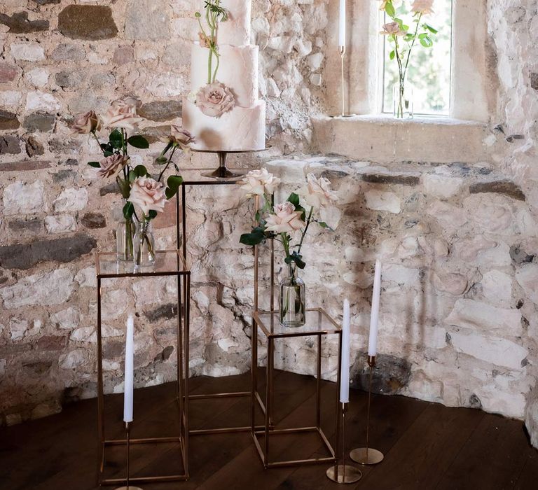 Fairytale wedding cake with four tiers, buttercream icing, and garden rose and stem decorations on brass cake stand on three tiered decor with garden roses and tapered candles at Pentney Abbey wedding 