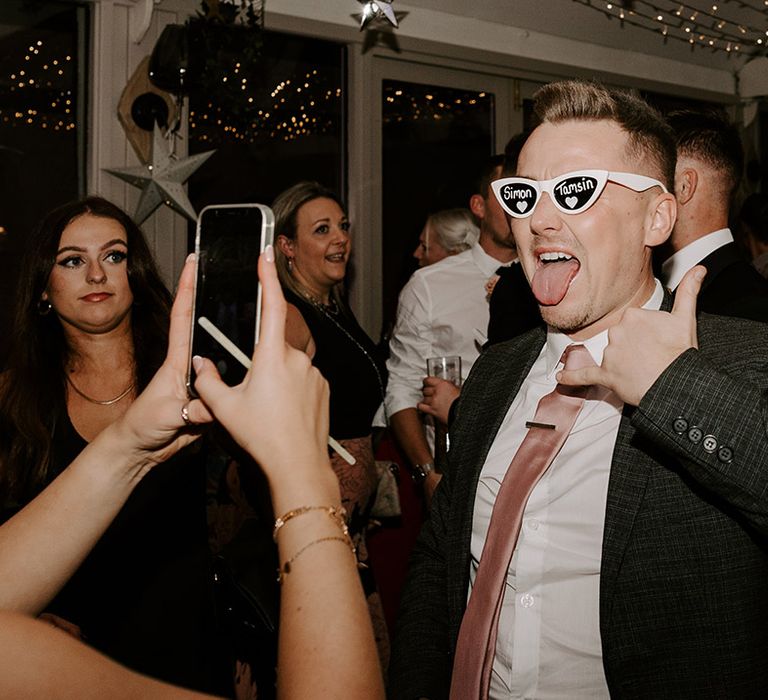 Wedding guest wearing white retro sunglasses with painted names of the bride and groom on each lens 