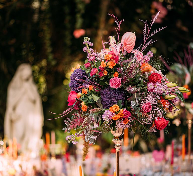 Tall colourful floral centrepieces with pink heart table name and menu signage on round tables 