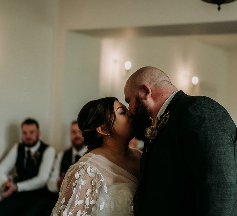 Groom in green tweed wedding suit kissing bride for the first time as a married couple