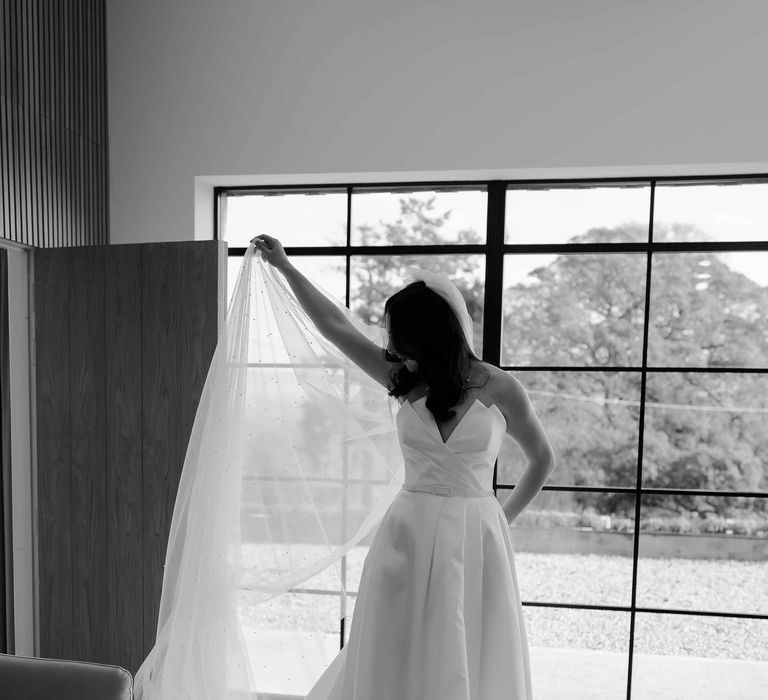 Bride in silk weding dress with sweetheart neckline holding her bridal veil