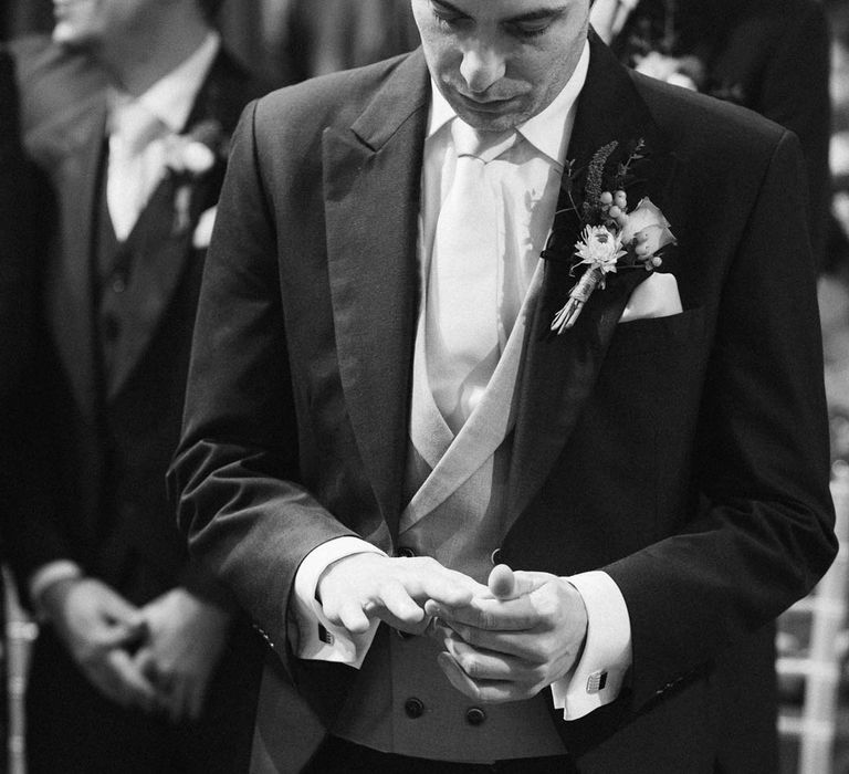 Groom wearing navy grooms morning suit with grey waistcoat, off-white tie and mixed wildflower boutonniere at the alter of South Farm wedding venue