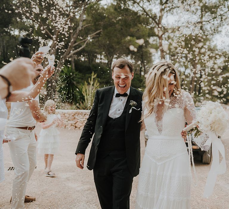 confetti moment with groom in a black tuxedo and horseshoe waistcoat and bride in a boho lace wedding dress smiling