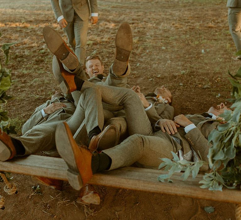 The groom and groomsmen fall on top of each other as they fall off the wooden swing 