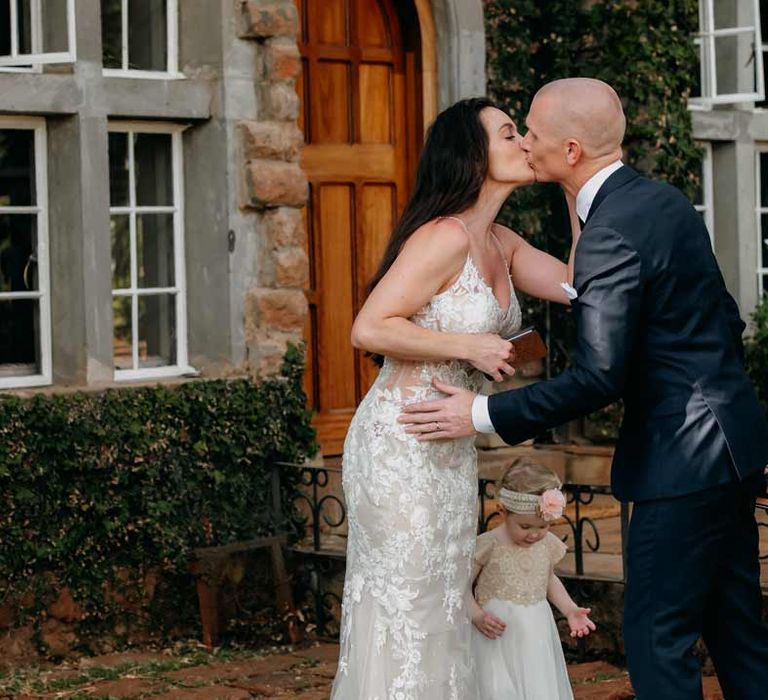 Groom in classic black grooms suit kissing bride in lace sleeveless wedding dress with puddle train at elopement at Giraffe Manor wedding venue