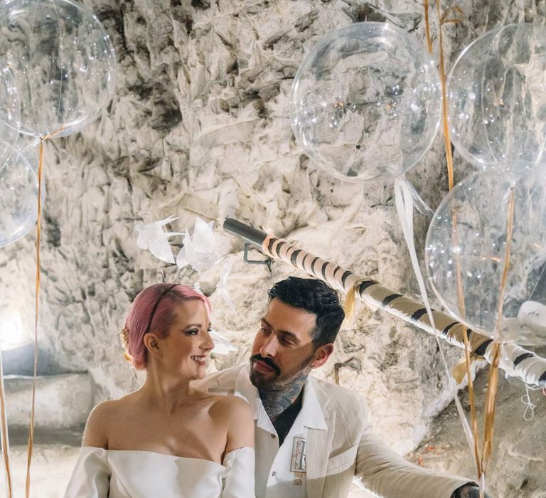 Bride in alternative off the shoulder puff sleeve short wedding dress and white chunky wedding boots sitting with groom in beige linen suit and embroidered linen shirt on the steps at Margate Caves