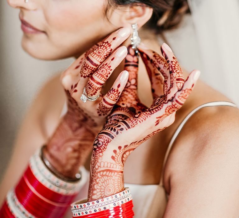 Bride with delicate wedding henna on putting on wedding earrings on her wedding day 