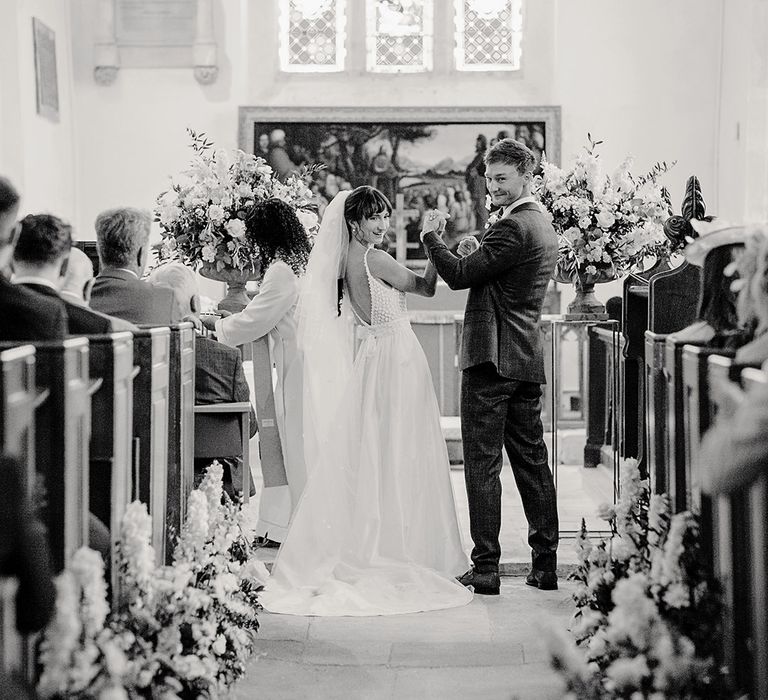 church wedding ceremony with aisle flowers and the bride and groom waving their arms in the air at the altar