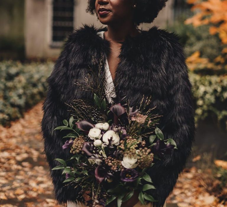 Bride in black faux fur cover up holding dark toned wedding bouquet 