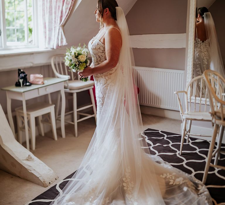 Bride in fitted floral lace wedding dress and veil holding white flower bouquet 