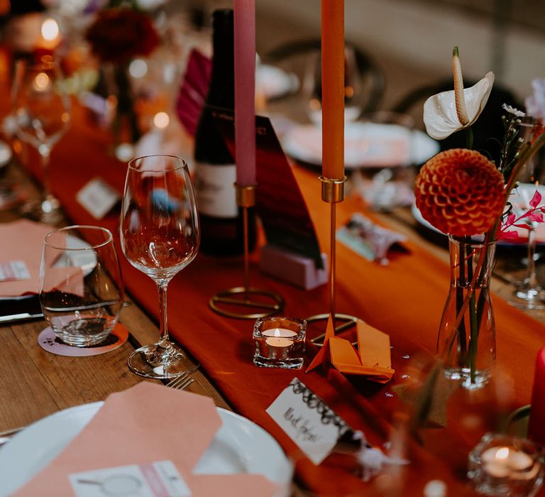 Pink and orange candles decorating wedding table with red table runner with heart origami napkins with place names and tea lights 