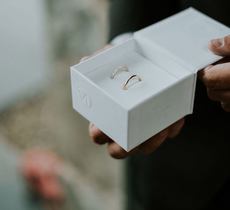 White ring box holding the bride and groom's gold wedding bands 