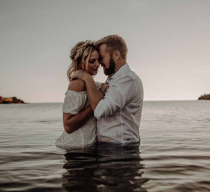 Bride in off the shoulder dress and groom in shot in the sea as they share an embrace