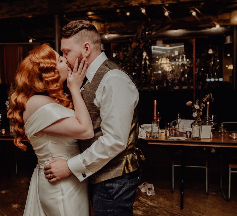 Bride with vintage wedding hair kissing her groom at evening reception 