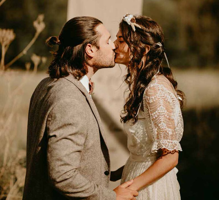 Bride and groom kiss in front of a paper sign at their sustainable wedding