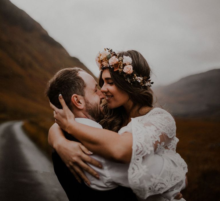 Bride in pink rose flower crown and groom kiss outside at highland wedding in Glencoe