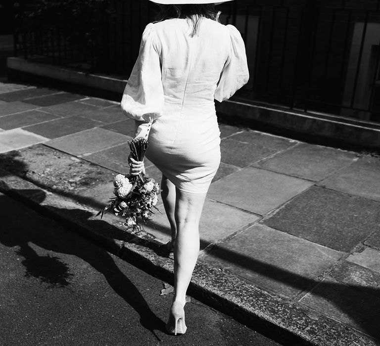 Black and white photography of bride walking down London street wearing short long sleeve wedding dress