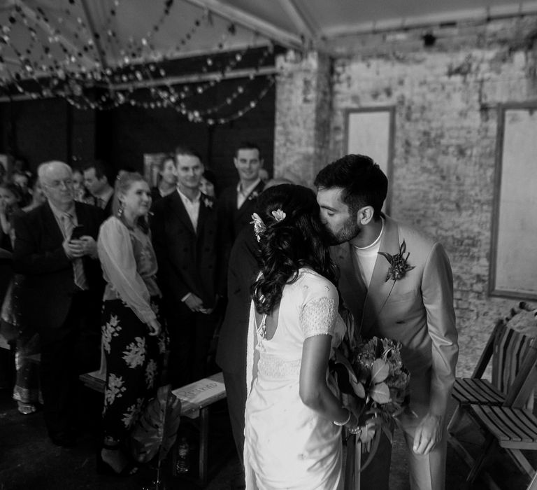 Black and white portrait of the groom kissing his bride in a sari at the altar 