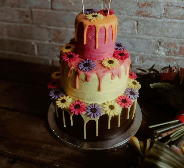 Colourful drip wedding cake with iced flower design and gold glitter cake topper 