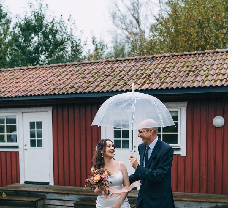 The bride and groom huddled under an umbrella in the autumn rain