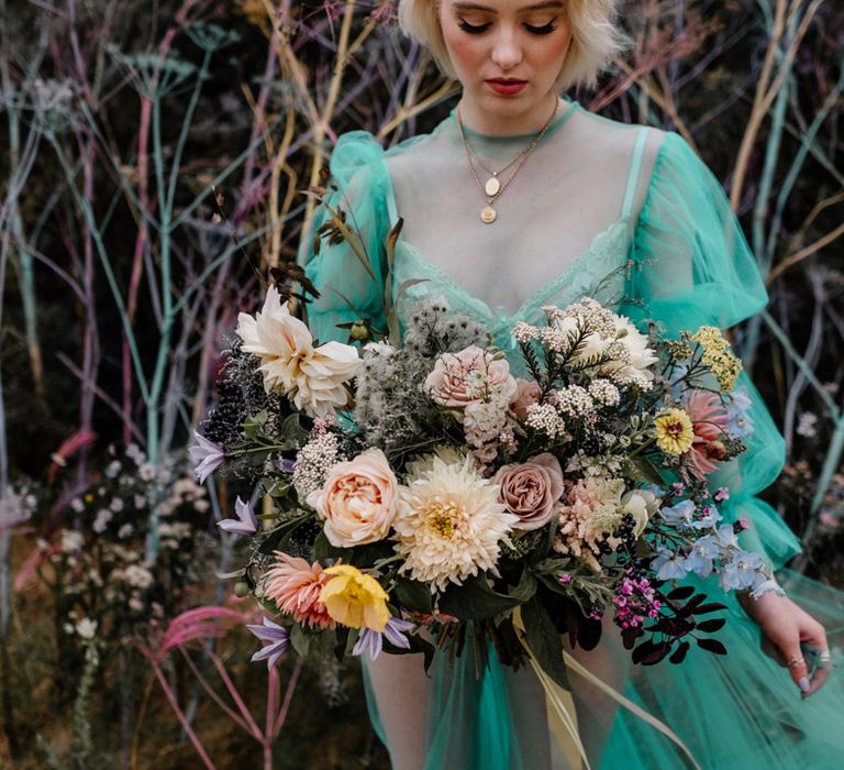 Bride holding a colourful rose, dahlia and foliage wedding bouquet 