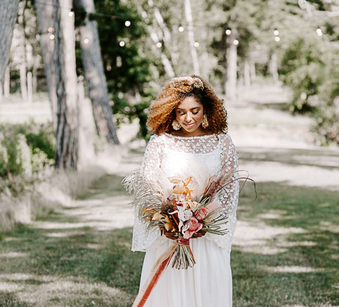 Bride holds brightly coloured dried floral arrangement tied with ribbon