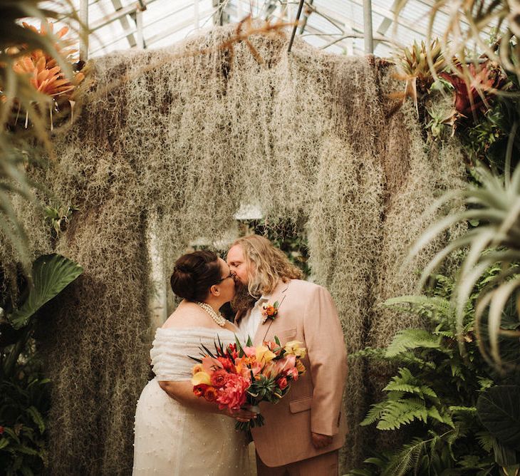 Stylish bride and groom kissing inside their greenhouse wedding venue 