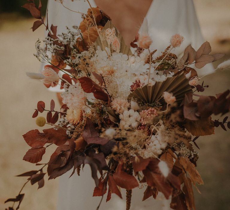 Bride holding an autumn wedding bouquet with brown leaves, dried palms, and white flowers 