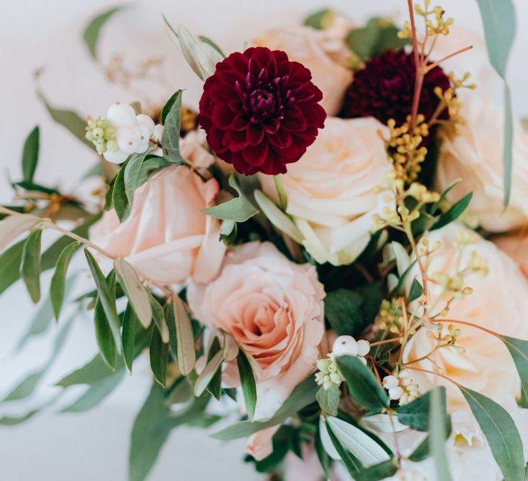 A bouquet of dark red dahlias, white and blush pink roses, olive leaves and wild foliage