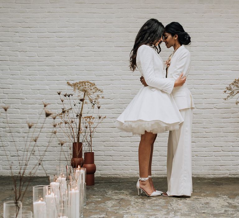 Two brides at the top of a candlelit aisle for all white wedding ceremony, with couture bridal outfits