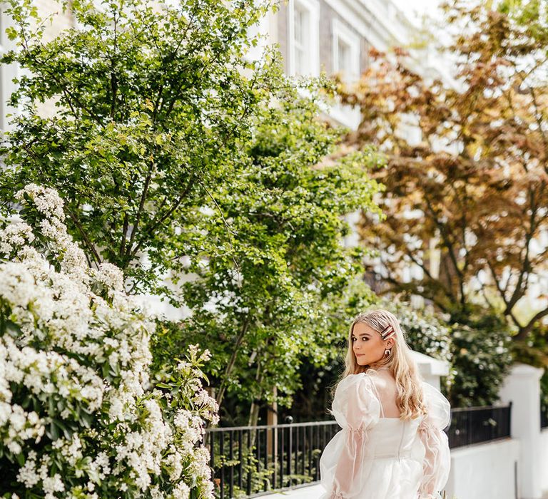 Bride in a short ruffle wedding dress with sheer long sleeves and brown boots holding her citrus bouquet behind her back 